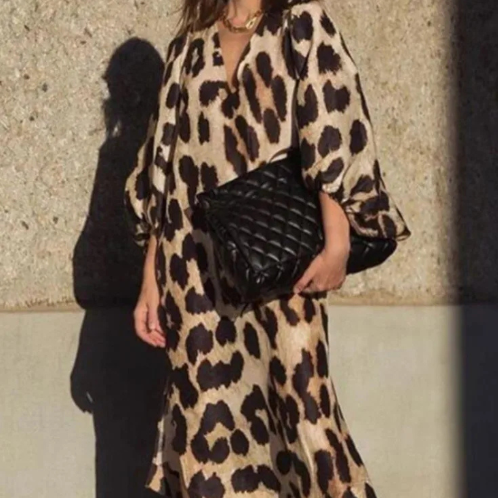 Frau in Leopardenkleid mit schwarzer, gesteppter Clutch vor Betonwand.