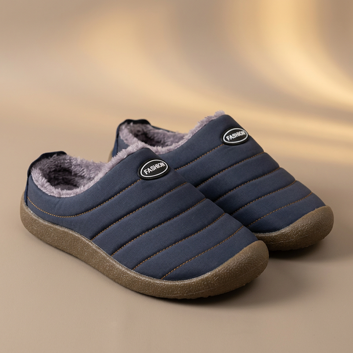 Pair of navy blue quilted slippers with gray fleece on a warm beige studio backdrop 18