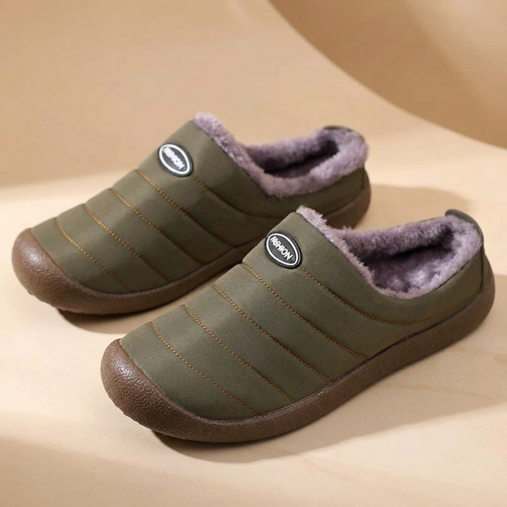 Pair of olive green quilted slippers with lavender-gray fleece on a beige curved backdrop 17