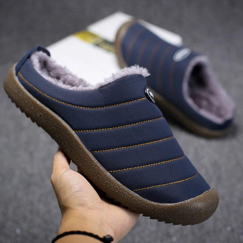 Hand holding a navy blue slipper, showing orange stitching, thick sole and soft lining 6