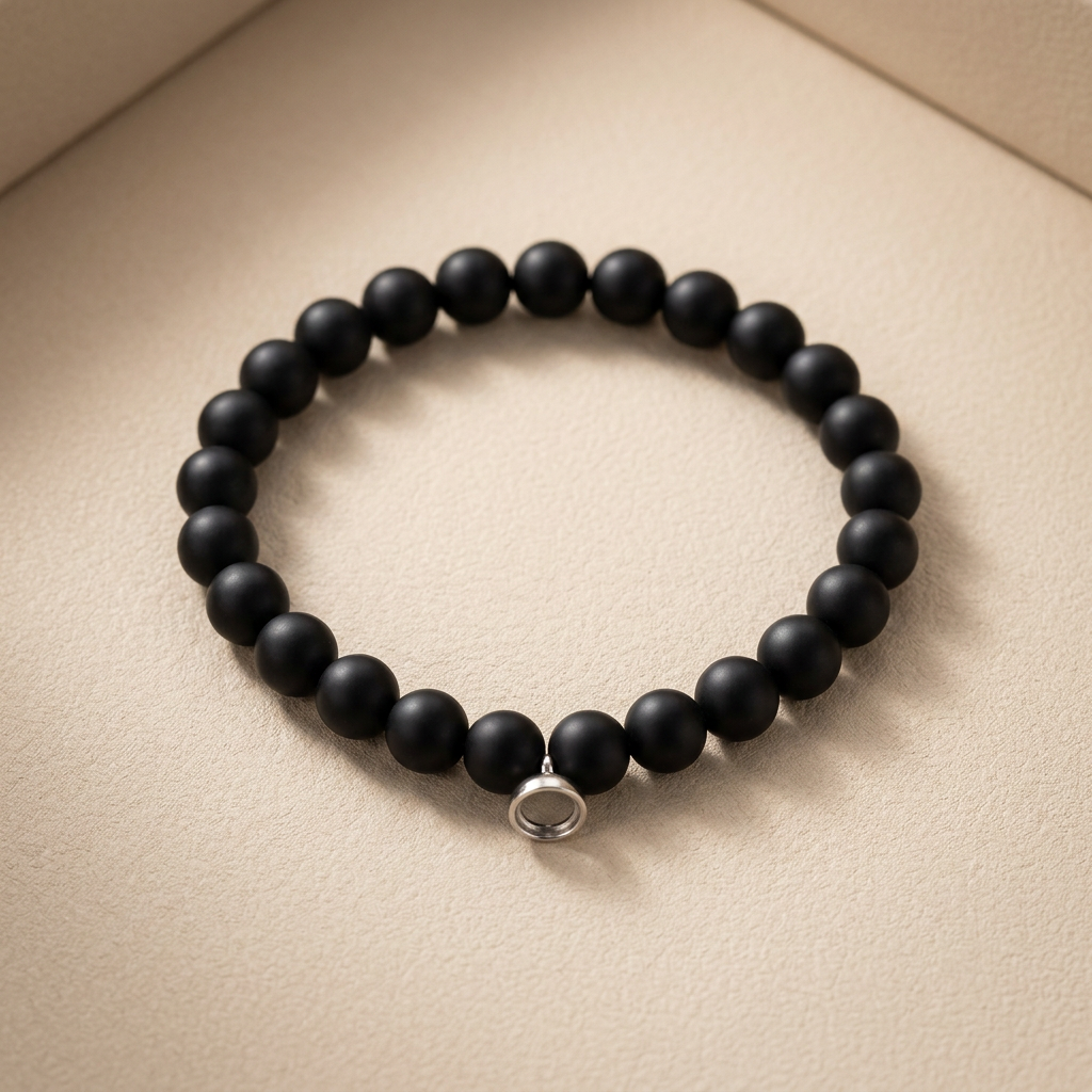 Stretch bracelet of matte black round beads with a small silver ring charm, on beige 1