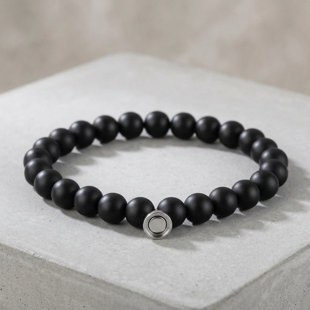 Matte black bead bracelet with a silver-tone round clasp, displayed on a pale concrete block 2