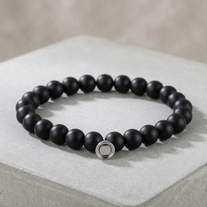 Matte black bead bracelet with a silver-tone round clasp, displayed on a pale concrete block 2