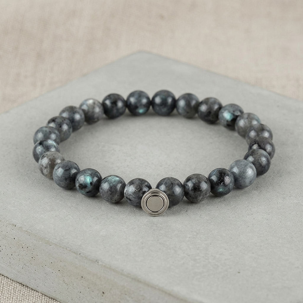 Dark gray bead bracelet with blue-green flashes and a round metal clasp on a concrete slab 4
