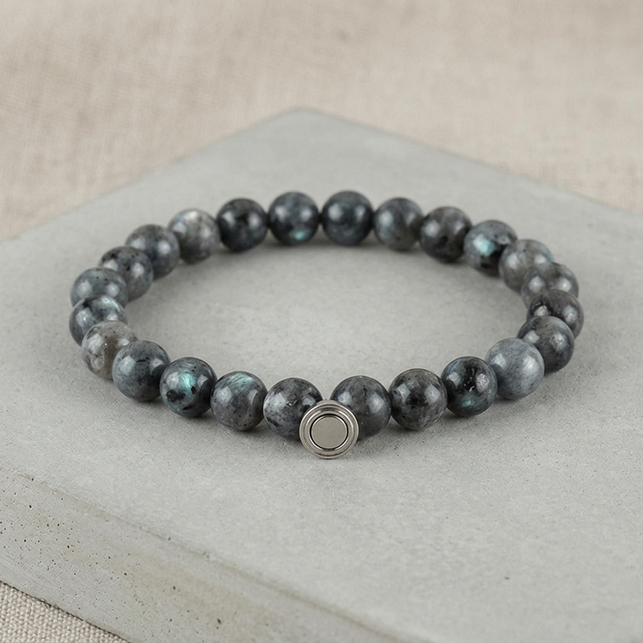 Dark gray bead bracelet with blue-green flashes and a round metal clasp on a concrete slab 4