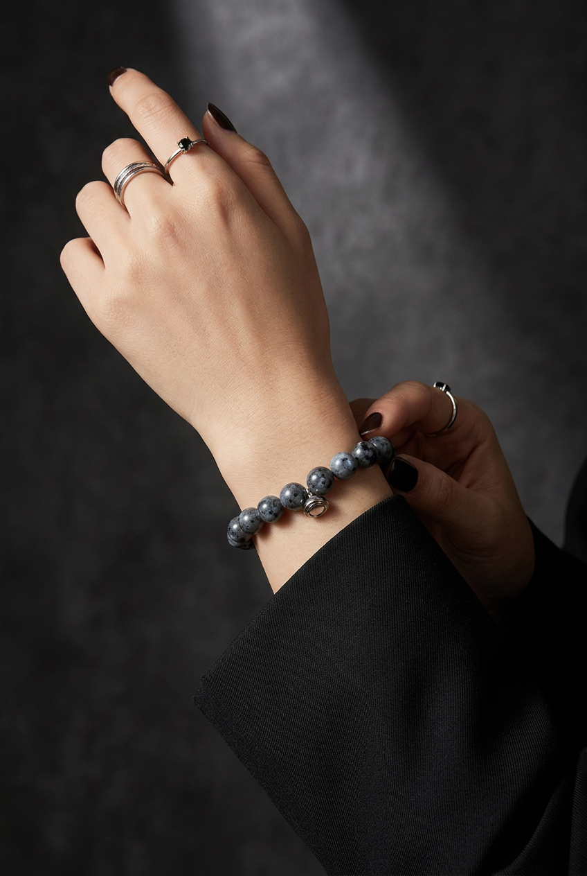 Woman's wrist wearing a gray speckled bead bracelet with silver clasp, shown with rings against a dark background 4