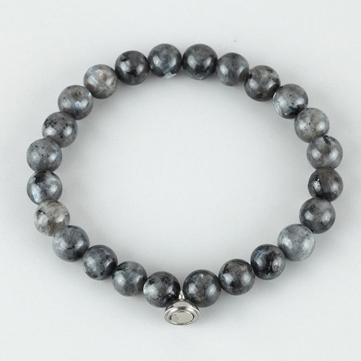 Flat lay of a bracelet of dark gray speckled round beads with a silver clasp charm 4