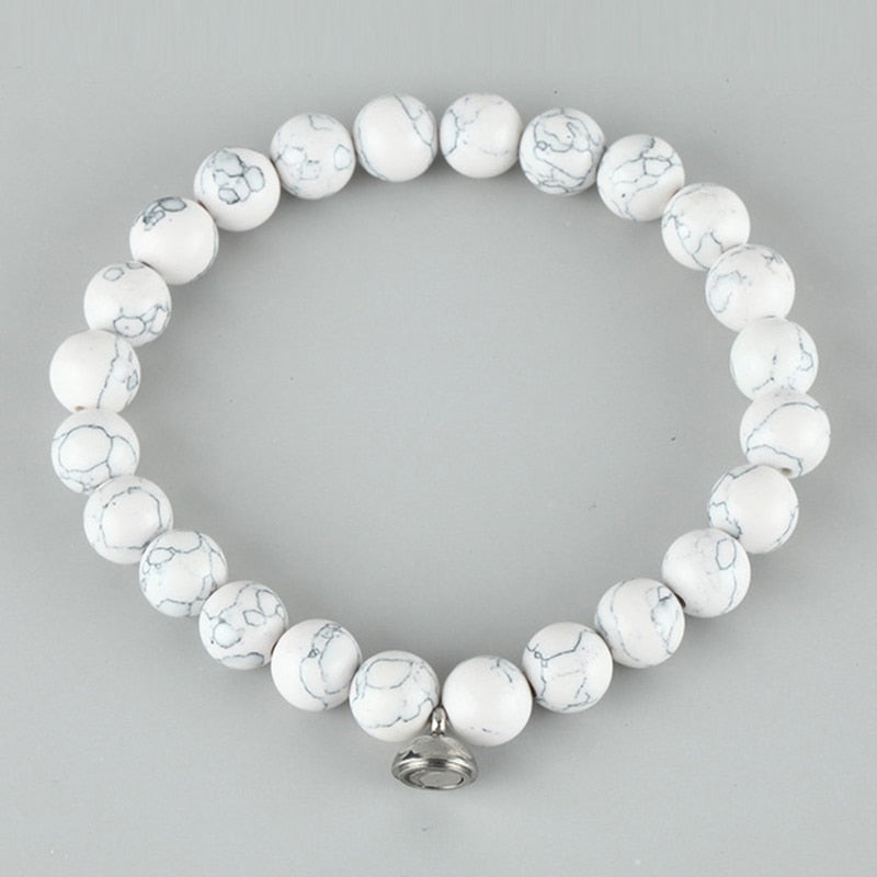 Flat lay of a bracelet of white round beads with gray veining and a silver clasp charm 3