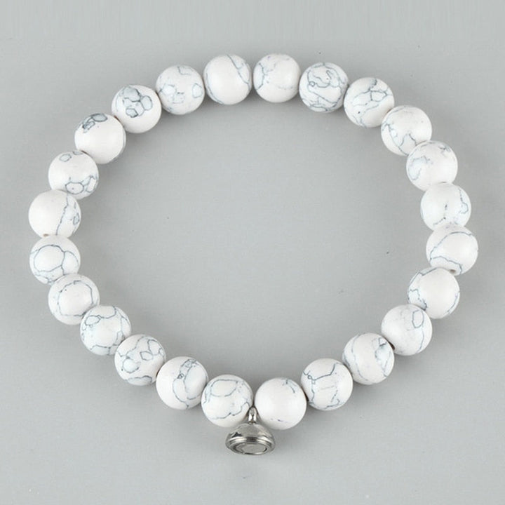 Flat lay of a bracelet of white round beads with gray veining and a silver clasp charm 3