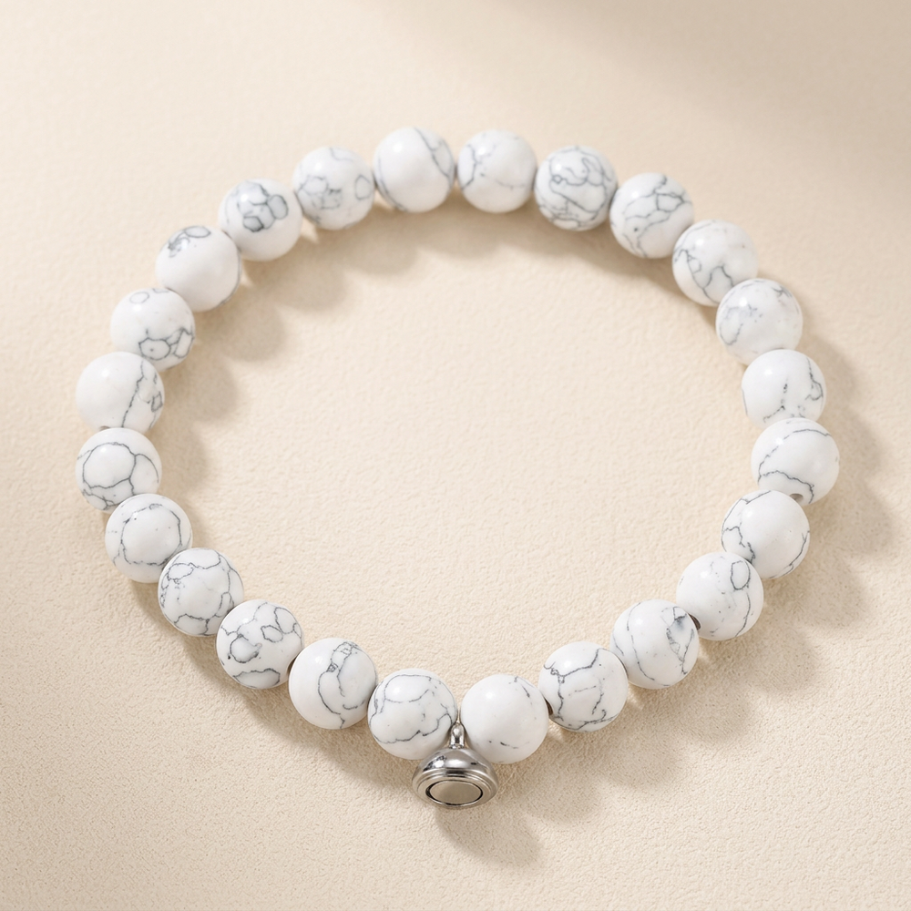 Bracelet of white beads with gray marbled veining and a silver magnetic clasp, on a cream surface 2