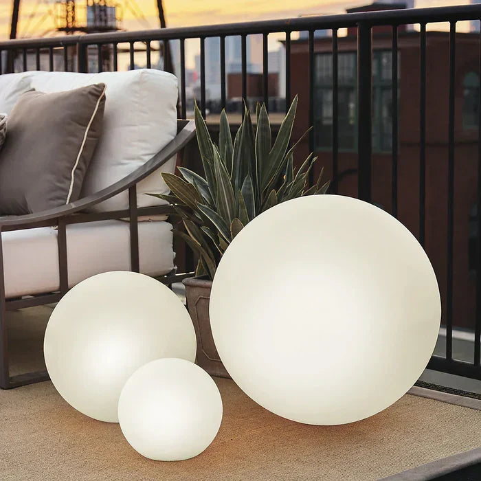 Three white spheres of different sizes on a balcony beside a cushioned outdoor chair and potted plant 12