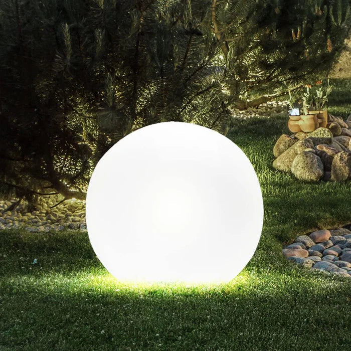 Single large white sphere glowing on a lawn near pine branches, rocks and pebbles 13