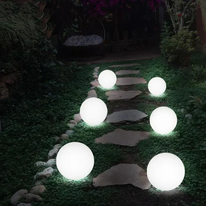 Six white glowing spheres of mixed sizes lining a flagstone path through a dark garden 15