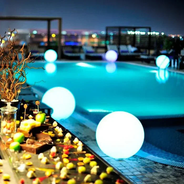 Glowing spheres beside a rooftop swimming pool at night, with a food display in the foreground 17