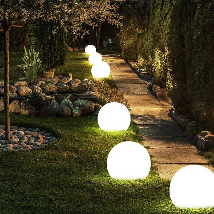 Row of lit white spheres along a lawn beside a stone garden path at night 2
