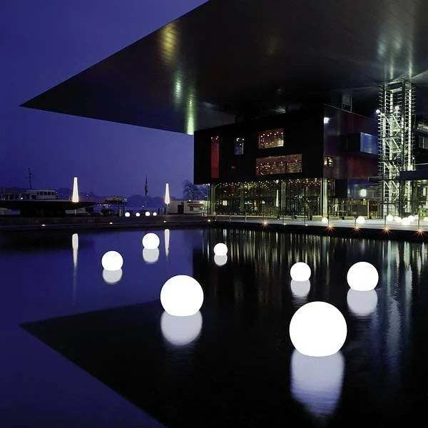 Glowing white spheres floating on dark water in front of a modern building at night 20