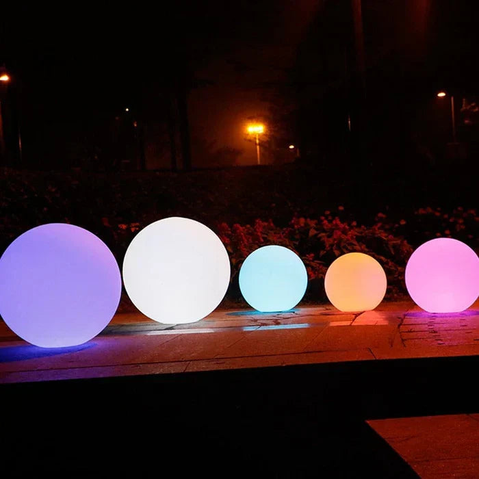 Five spheres in graduated sizes glowing purple, white, blue, orange and pink along a paved edge 5