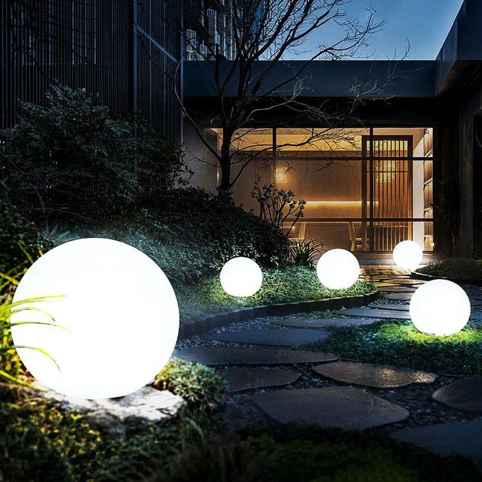 White glowing spheres of varied sizes along a stepping-stone path in a landscaped garden at dusk 7