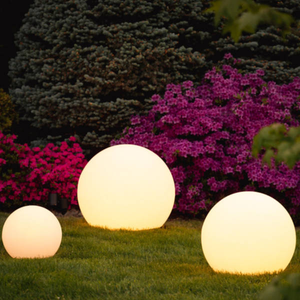 Three warm-glowing spheres on grass in front of pink flowering shrubs and an evergreen tree 9