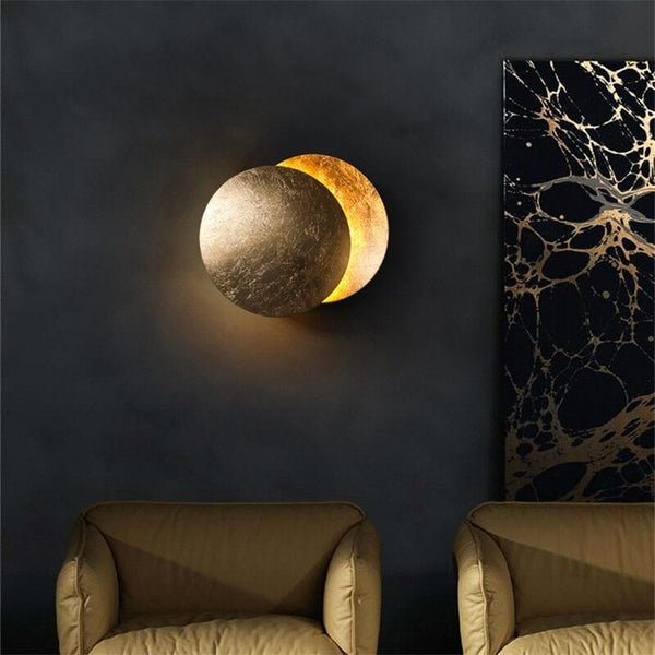 Lit gold moon wall lamp on a dark wall above two armchairs, next to marbled artwork 6