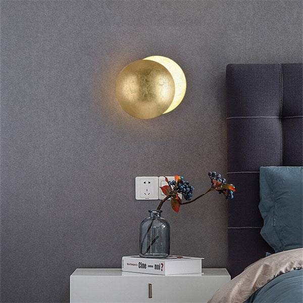 Brass-toned disc lamp on a gray wall above a white nightstand with a vase of berries 7