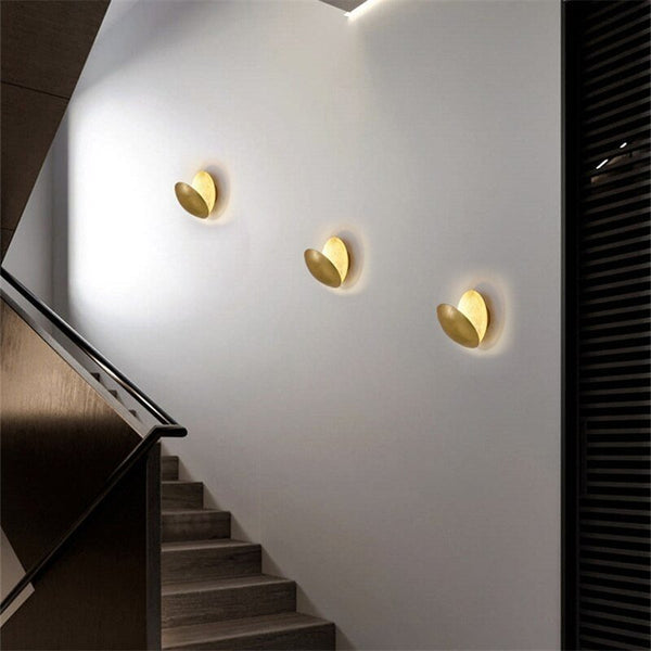 Three gold lamps angled in a row on a white stairwell wall, casting soft halos of light 8