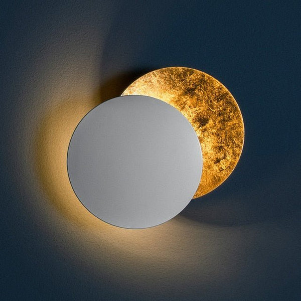 White front disc over a gold-leaf disc, glowing warmly against a dark blue wall 9