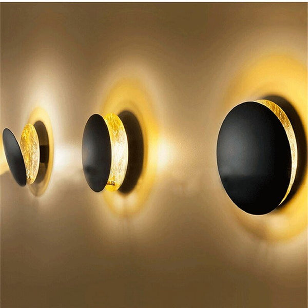 Three black-fronted discs with gold edges in a row, casting warm halos on the wall 10