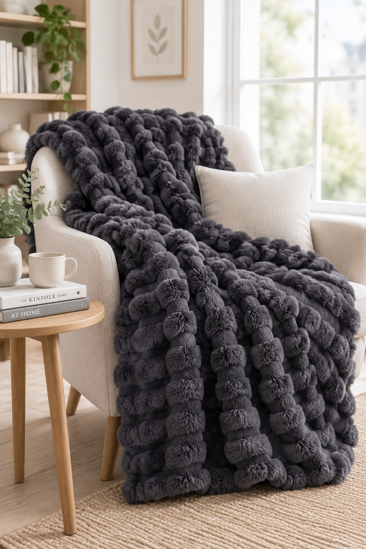 Charcoal gray pom-pom textured plush throw draped over a cream armchair next to a small wooden table 14