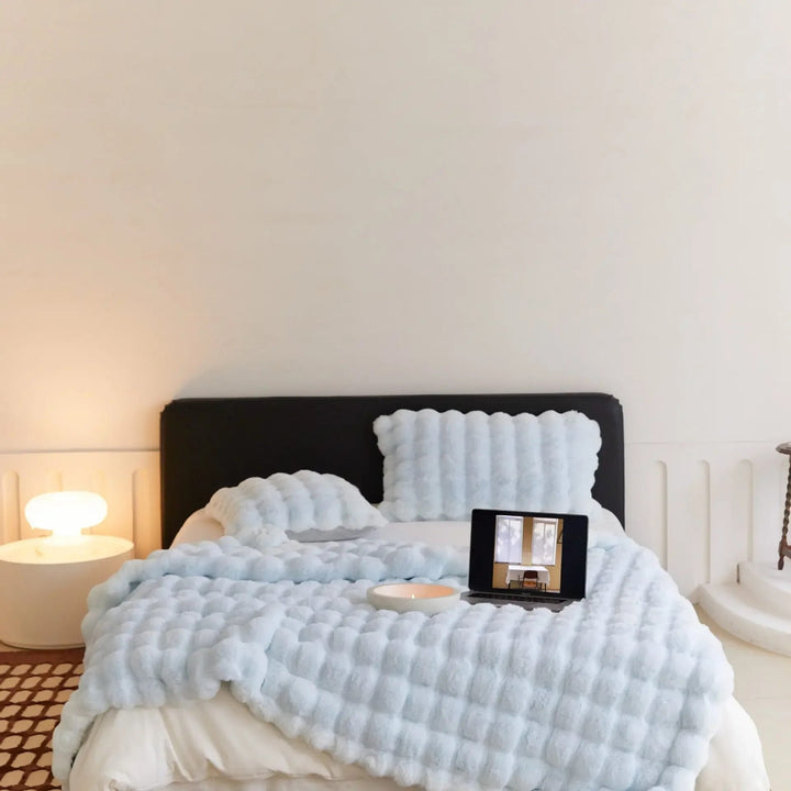 Pale blue plush throw and matching pillows on a bed with a laptop and candle bowl 6