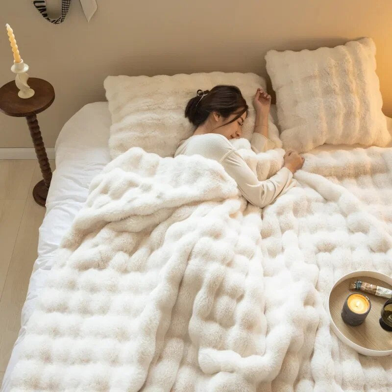 Woman asleep under a cream white plush throw, seen from above with pillows and a candle tray 12
