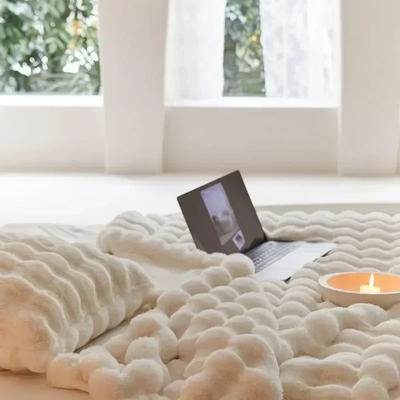 Close view of a cream plush blanket on a bed with a laptop and candle near a window 7