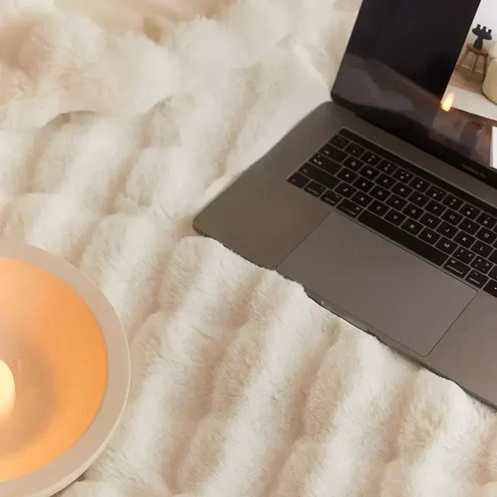 Top-down close-up of the soft cream plush surface beside a laptop and candle bowl 9