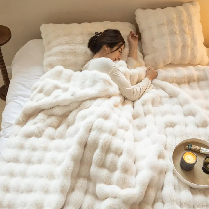 Woman sleeping under a cream white plush blanket with fluffy pillows and a candle tray beside her 5